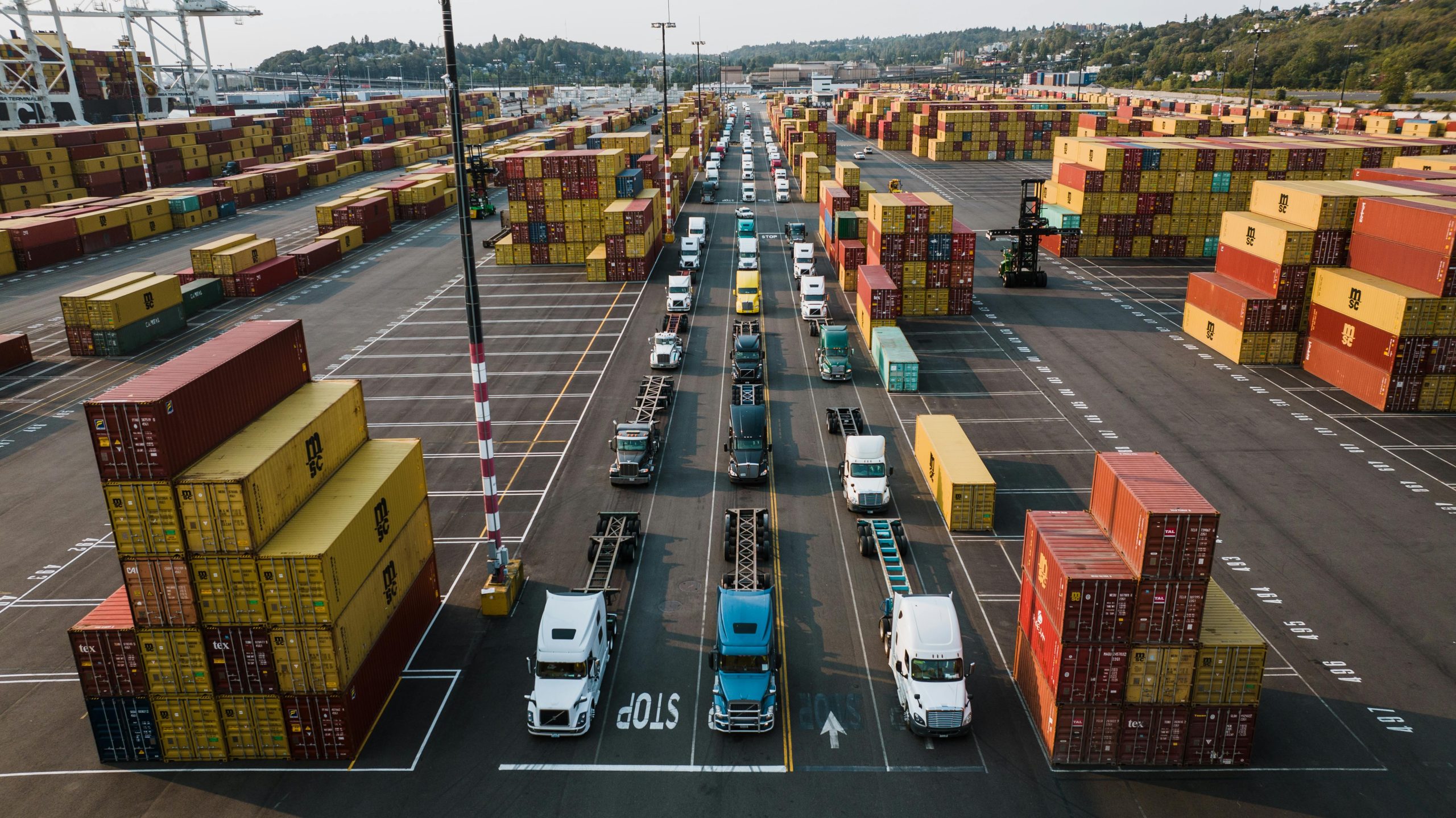 A bustling aerial shot of Seattle's shipping port with trucks lined up amongst colorful cargo containers.
