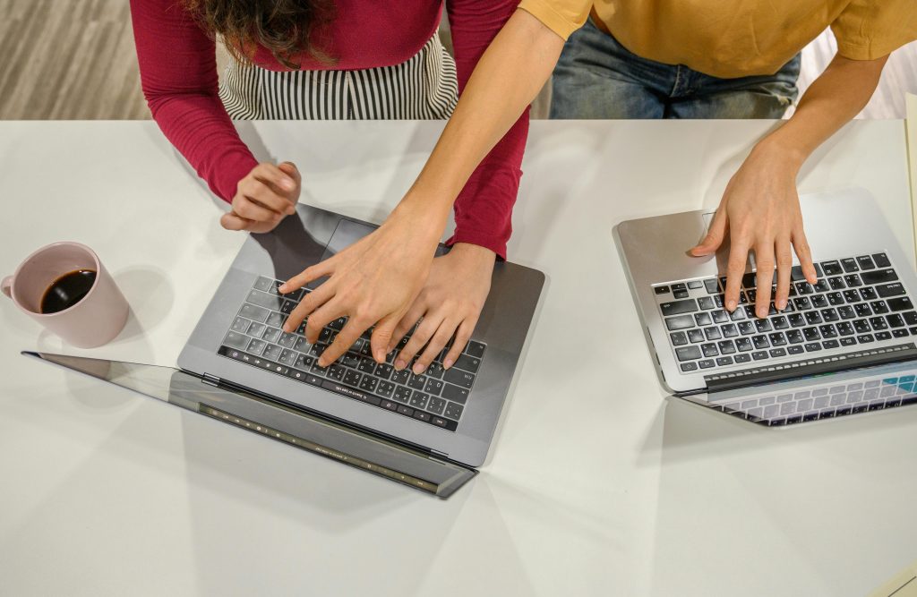 Two people collaborate on laptops with a cup of coffee in an office setting.